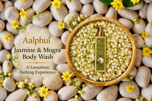Aalphul Jasmine & Mogra Body Wash bottle displayed in a gold bowl filled with white jasmine flowers, surrounded by smooth beige stones and small yellow blossoms. The left side features a semi-transparent oval overlay with product text.