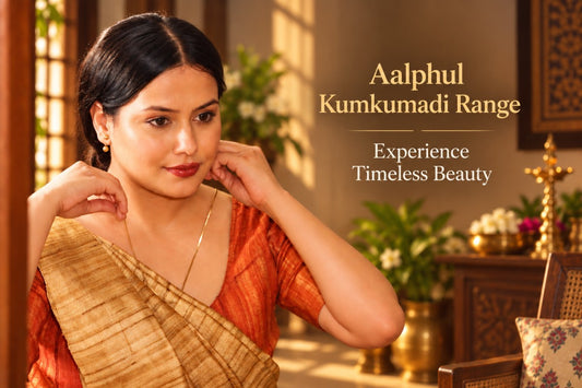 A woman wearing a traditional Indian saree with a gold and orange patterned blouse and a beige saree drape, posed in a warmly lit indoor setting with decorative plants and furniture. Text on the right reads 'Aalphul Kumkumadi Range' and 'Experience Timeless Beauty'.